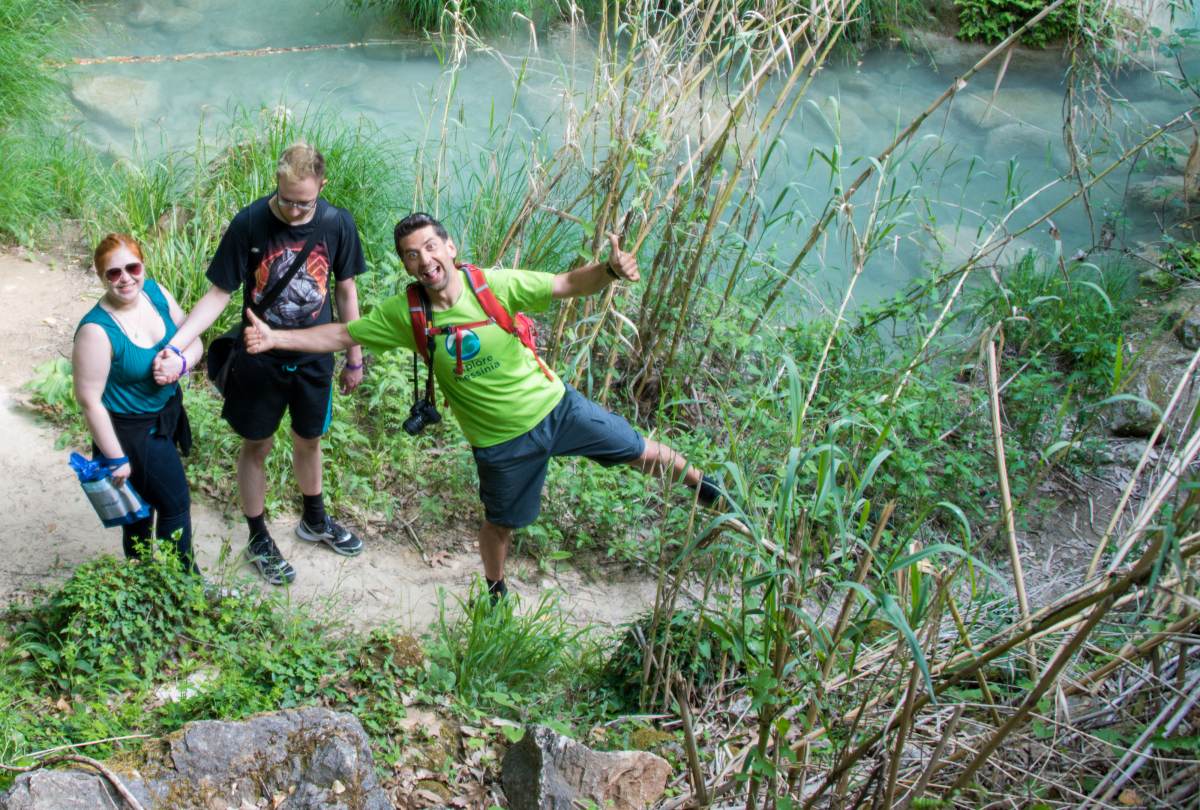 Three smiling hikers giving thumbs up on a trail above a green Polylimnio pool, one striking a playful pose