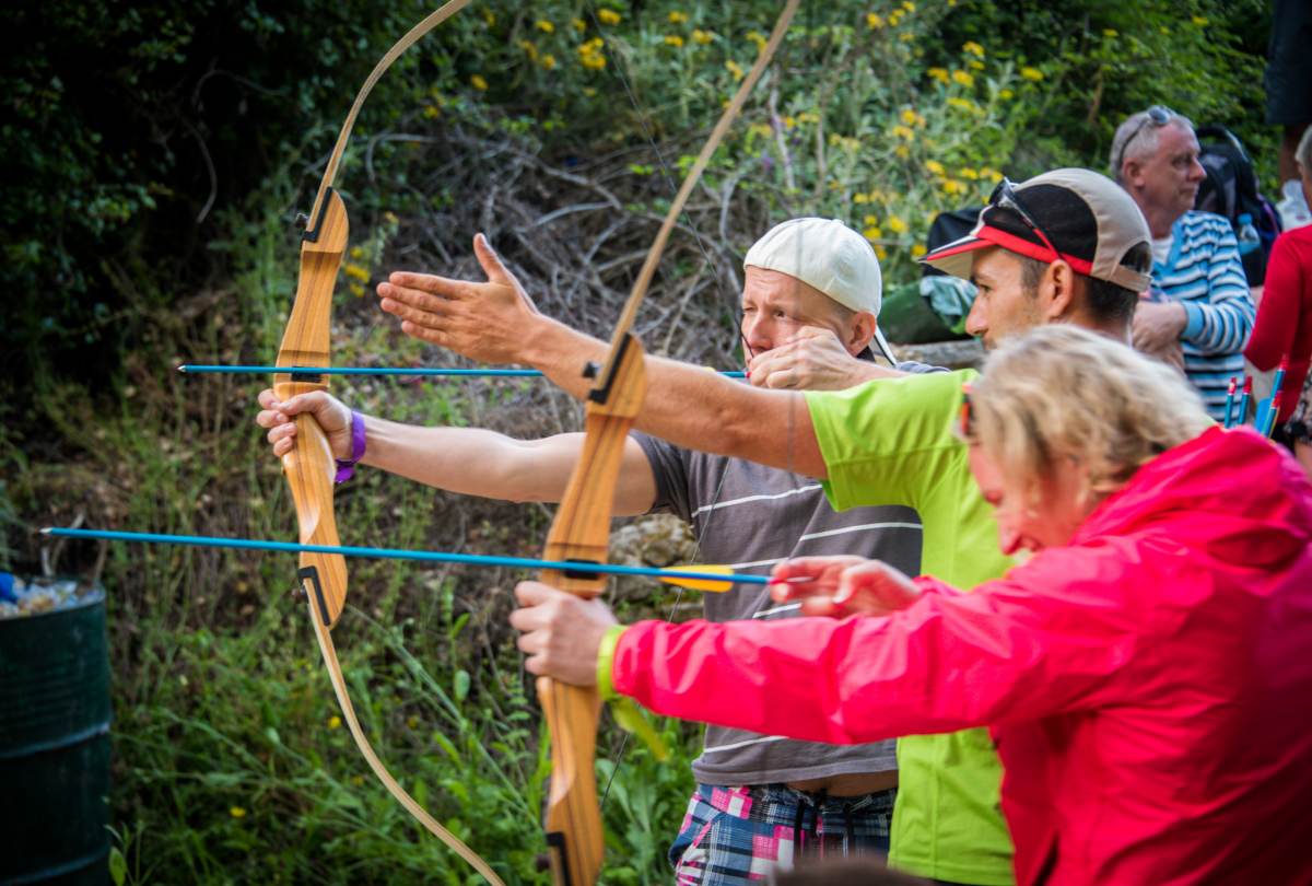 People aiming traditional wooden recurve bows during an outdoor archery session in the Messinian countryside