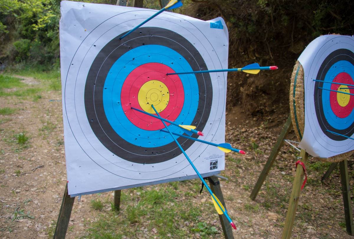 Colorful archery target boards stuck with blue and yellow arrows on wooden stands at an outdoor range