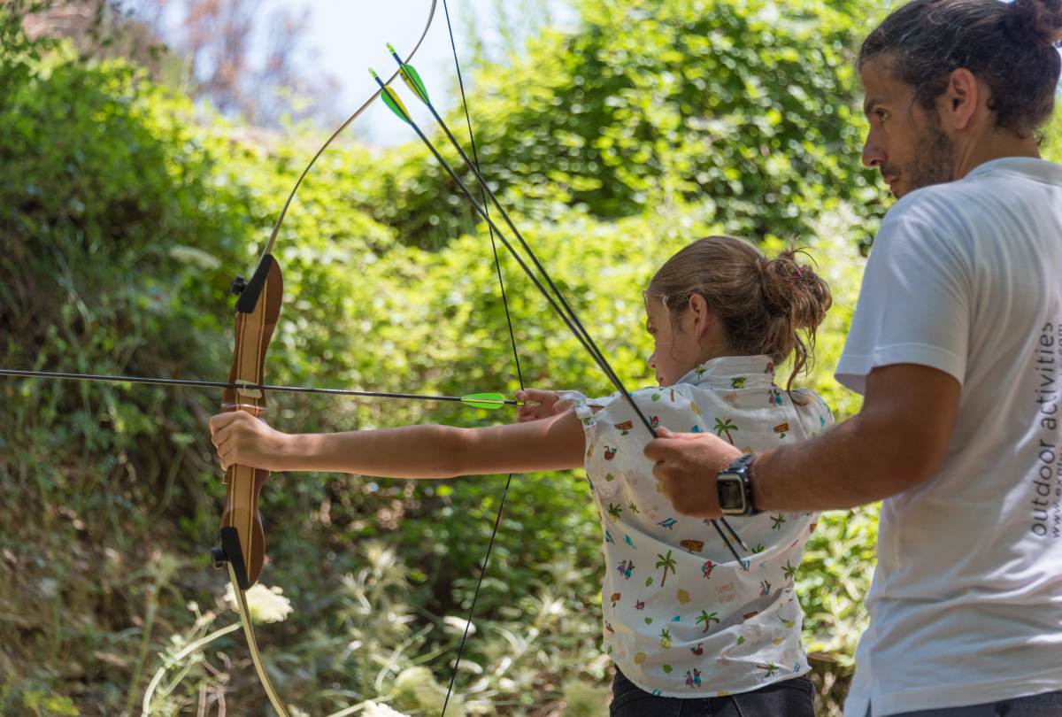 Guide helping a child aim a bow and arrow during outdoor archery at Polylimnio
