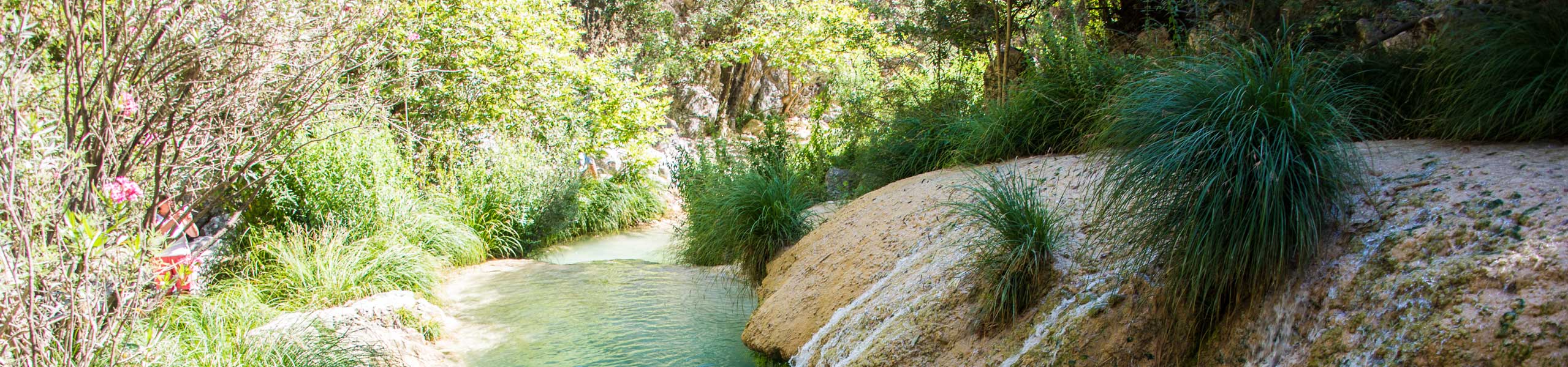 Panoramablick auf die üppige Polylimnio-Schlucht mit türkisfarbenen, gestuften Wasserfällen und natürlichen Pools in Messenien