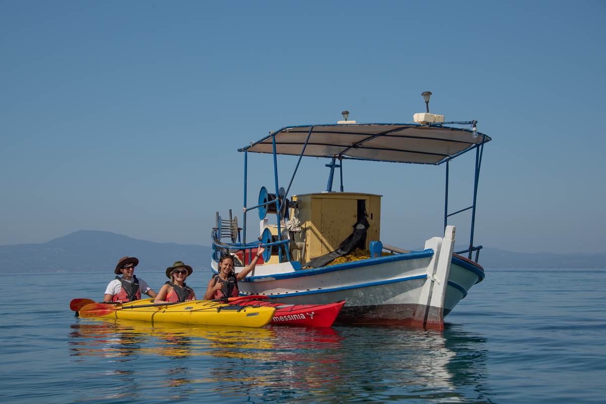 Peddelaars die zwaaien naast een traditionele houten Griekse vissersboot