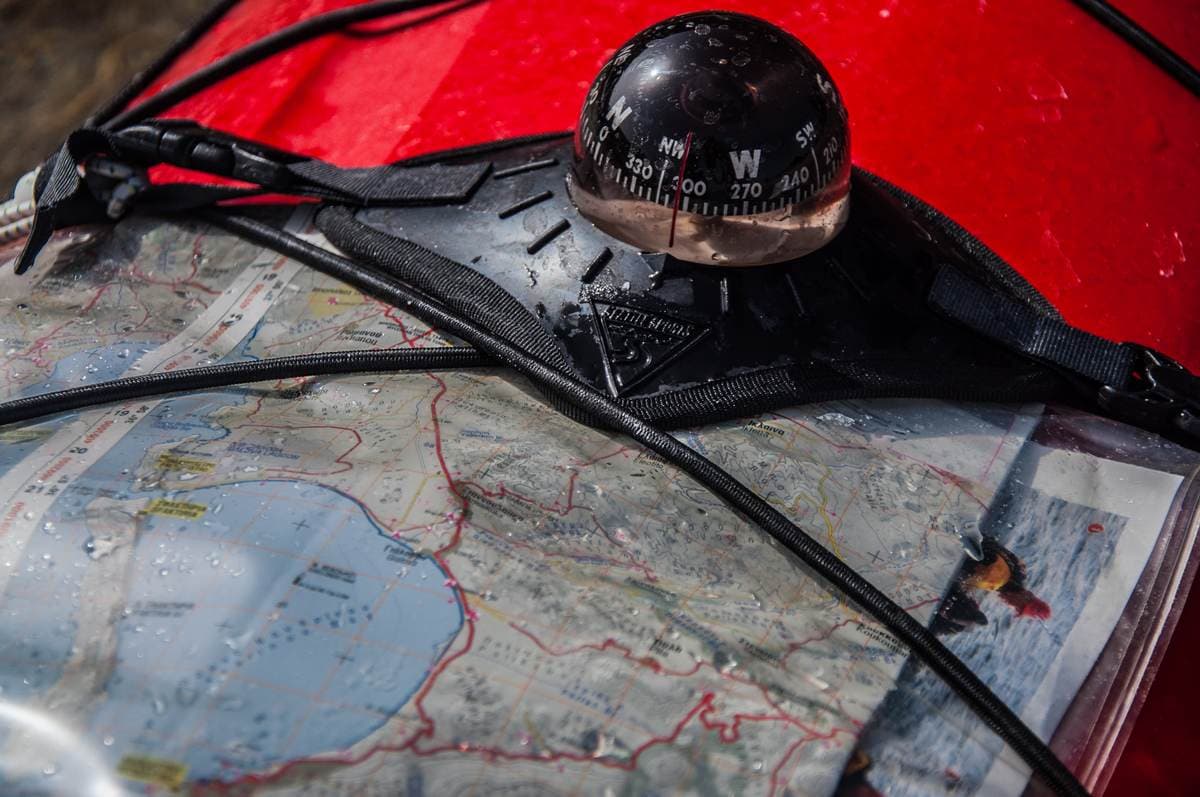 Navigatiekompas en topografische kaart op het dek van een rode kajak