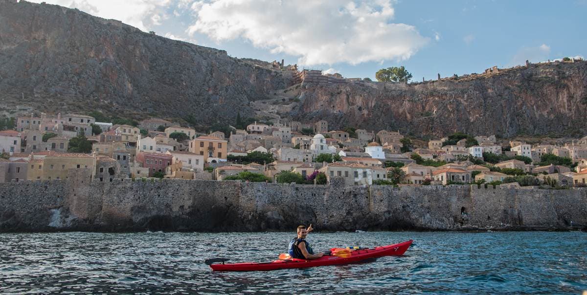 Ein Reisender paddelt in einem roten Kajak nahe der Stadtmauern beim Seekajakfahren in Monemvasia