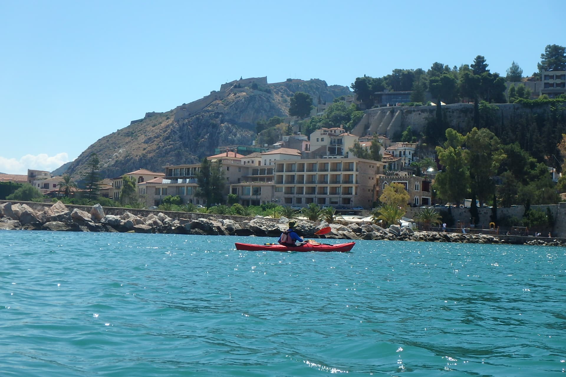 Kajakfahrer:in paddelt an der historischen Uferpromenade von Nafplio vorbei – bei einem Seekajak-Ausflug in Nafplio