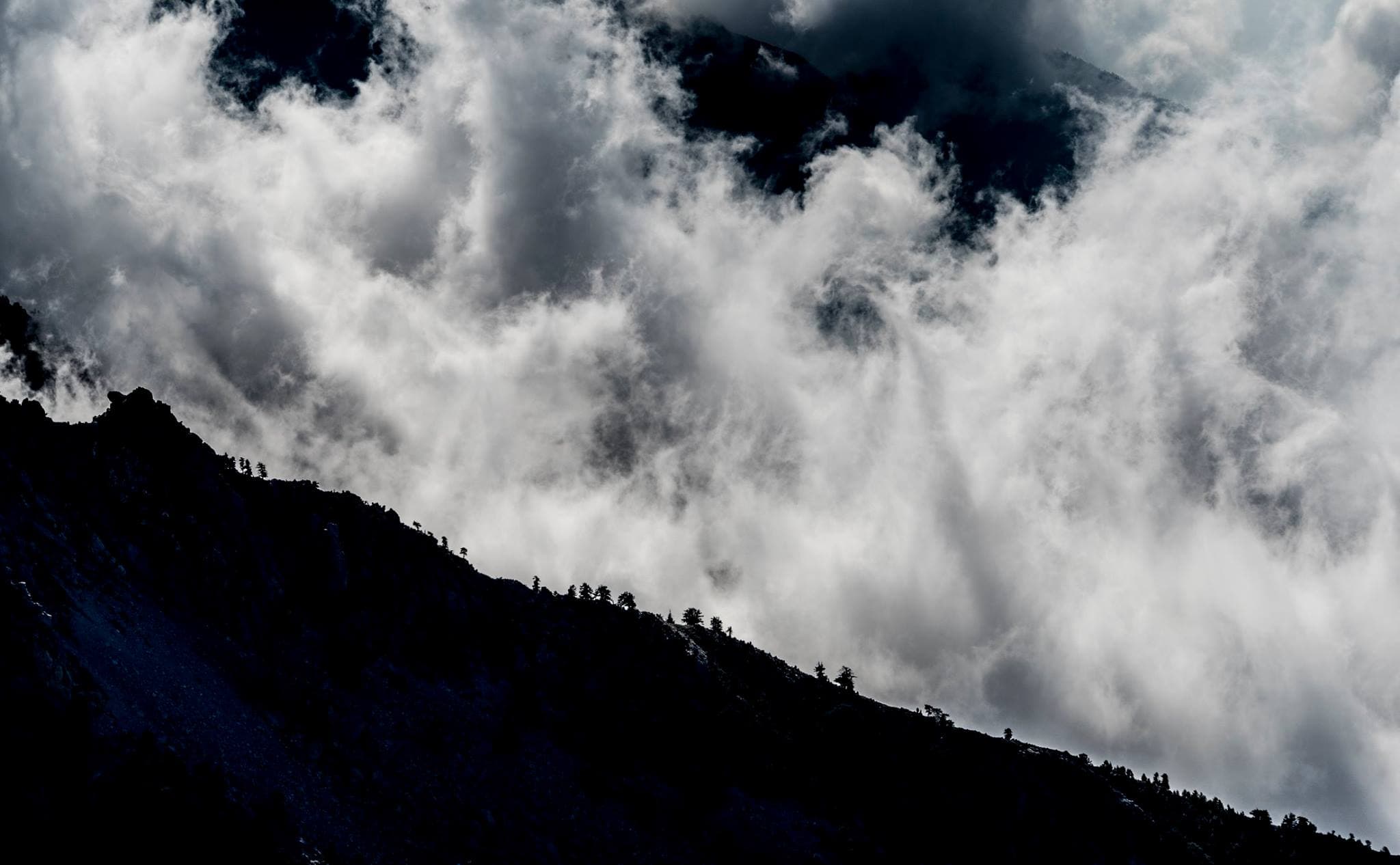 Silhouetted forested ridgeline of Taygetos with scattered pines wrapped in dramatic swirling clouds