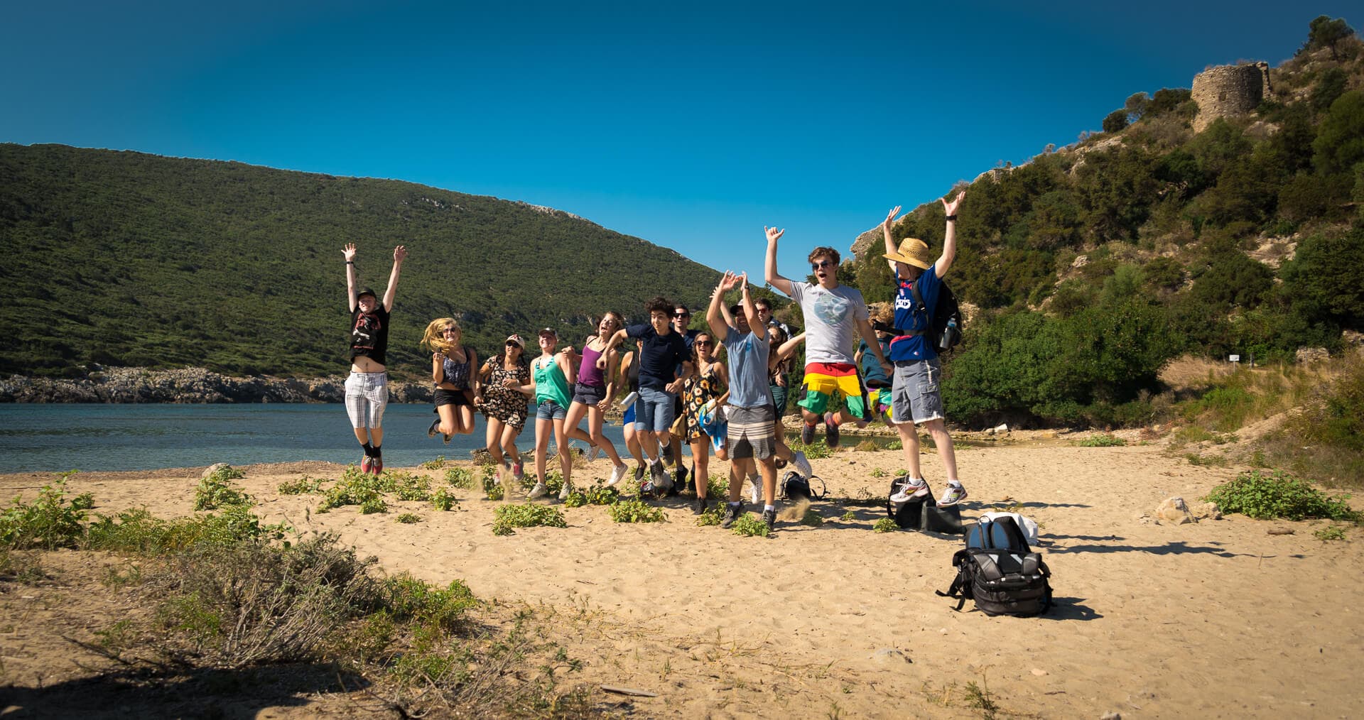Eine Gruppe von Schülern springt vor Freude an einem Sandstrand während einer der Outdoor-Bildungsreisen von Explore Messinia.