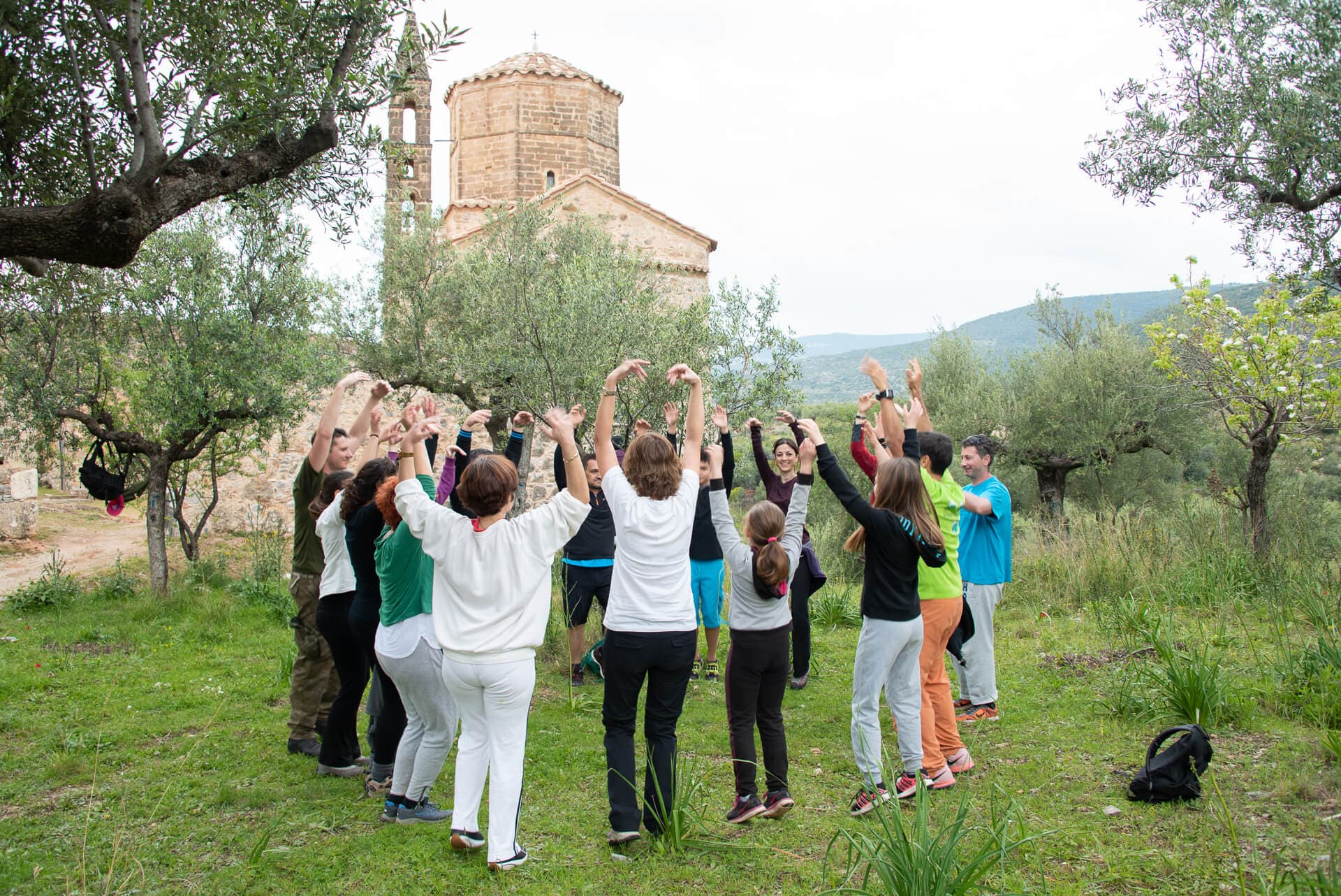 A student school group participating in a team-building circle near a Byzantine church.