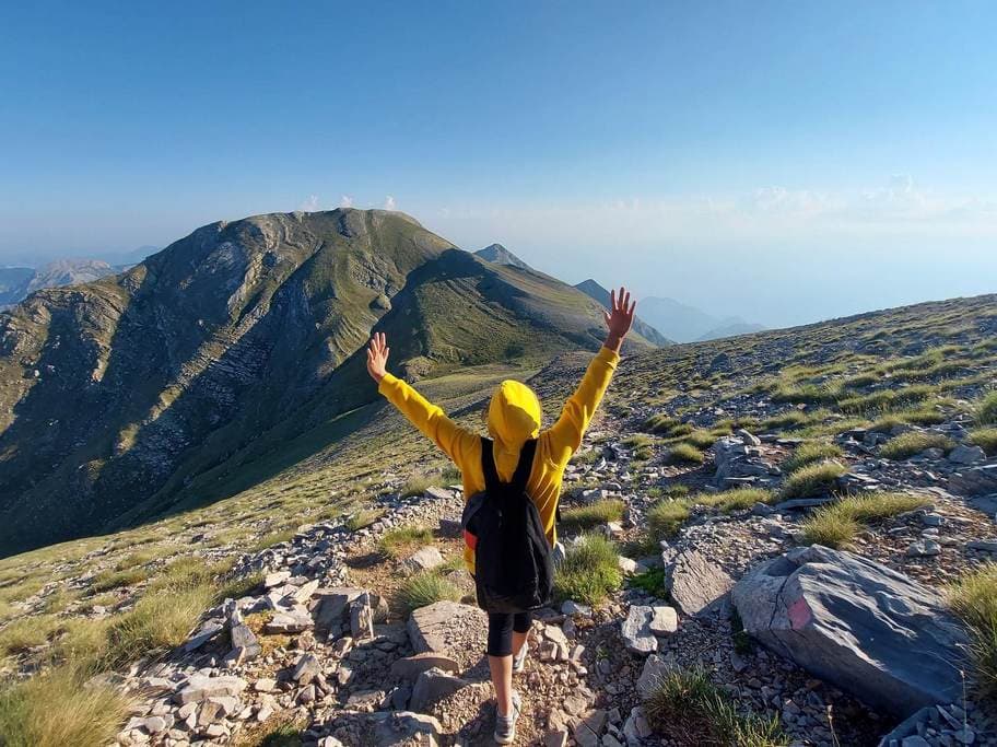 Begeleide wandelaar met de armen omhoog bij de stenen kapel op de 2407m hoge top van de Taygetos, Peloponnesos