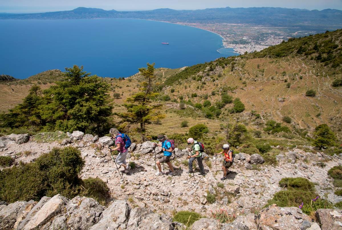 Four hikers descend a rocky ridge with sweeping views over Kalamata bay and the Messinian Gulf