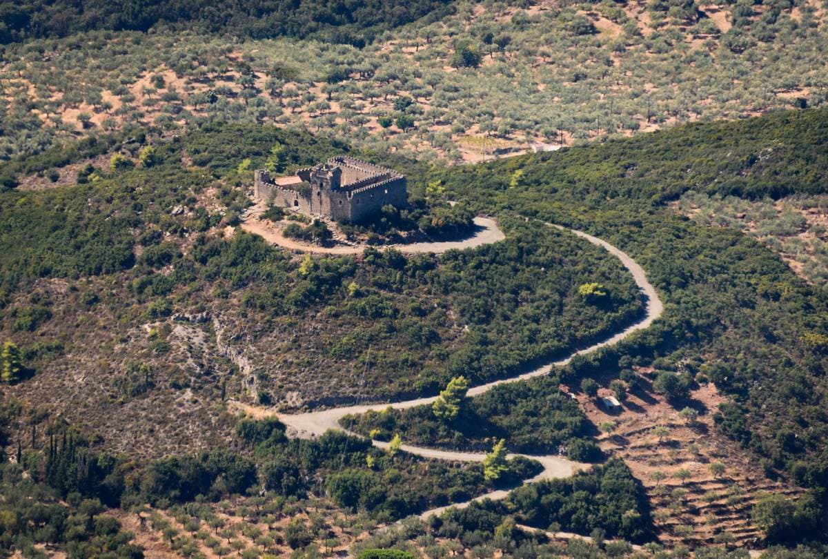 Stone mansion tower on an olive-grove hilltop reached by a winding dirt road in the Mani