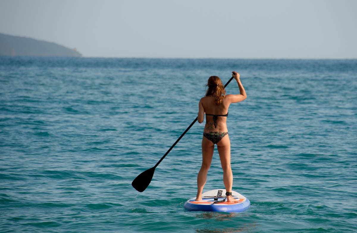Eine Person beim Stand-Up-Paddling auf dem klaren, türkisfarbenen Wasser der Voidokilia-Bucht in Messenien, Griechenland