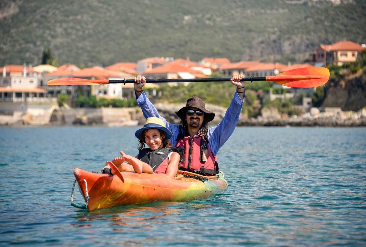 אב ובת מחייכים יחד בקיאק זוגי כתום על המים הכחולים והרגועים של קרדמילי.