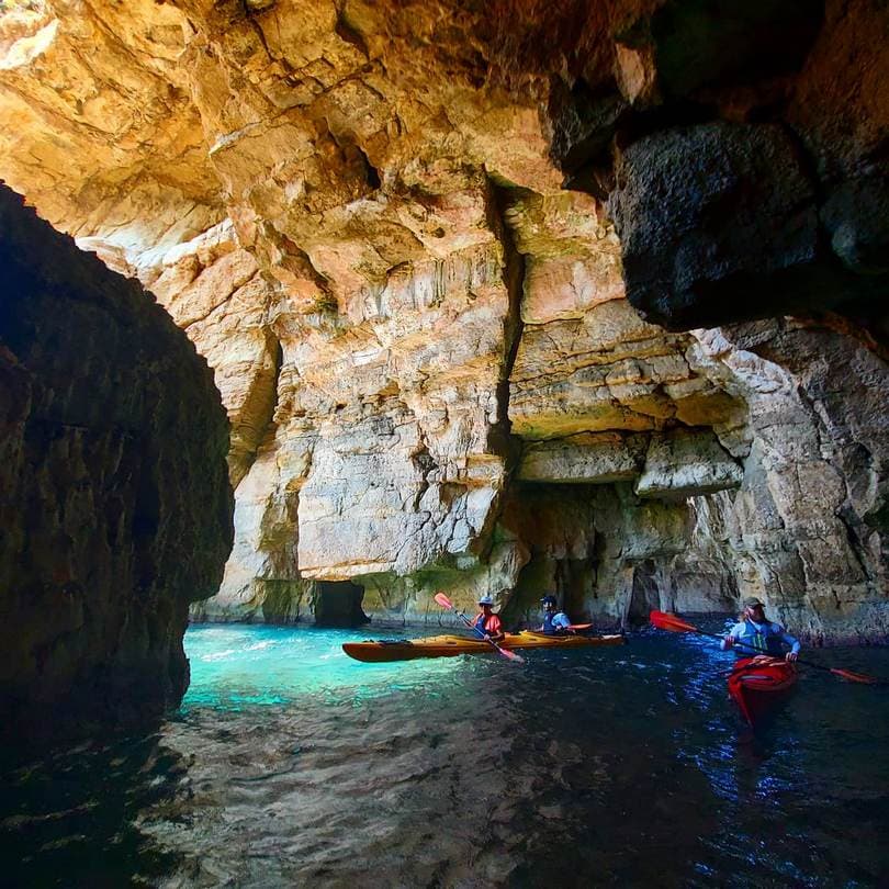 Kayakers exploring the vibrant turquoise waters inside a sea cave during sea kayaking navarino bay.