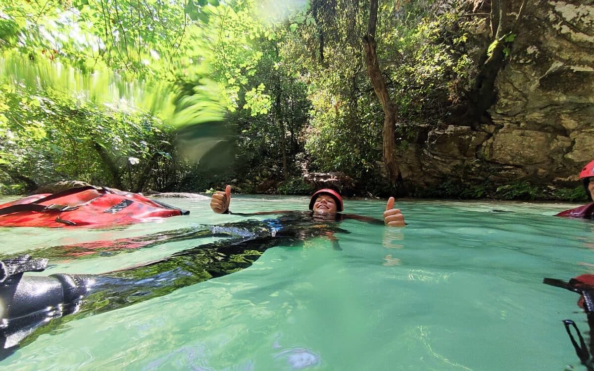 Canyoner floating in a green pool giving thumbs-up among trees at Polylimnio
