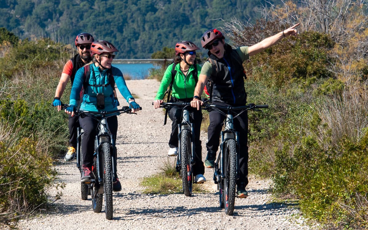 Eine fröhliche Gruppe genießt eine unserer geführten Radtouren in Griechenland auf einem malerischen Schotterweg an der Küste.