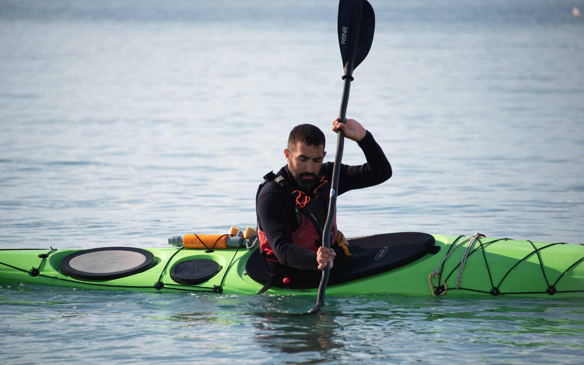 Paddler in a green sea kayak demonstrating efficient stroke technique on calm water.