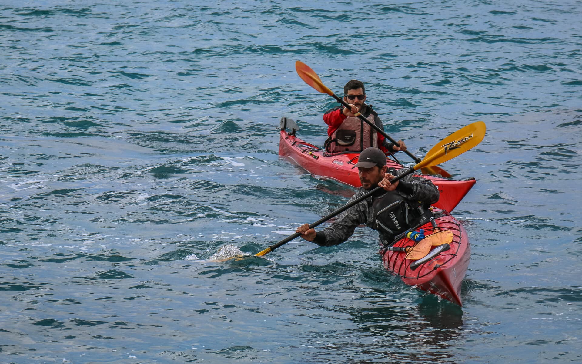 Two paddlers in sea kayaks moving across deep blue water during a group session.