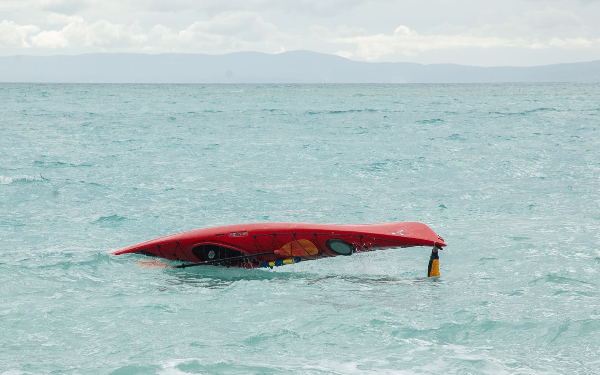A red sea kayak turned upside down during a controlled rolling and rescue drill.