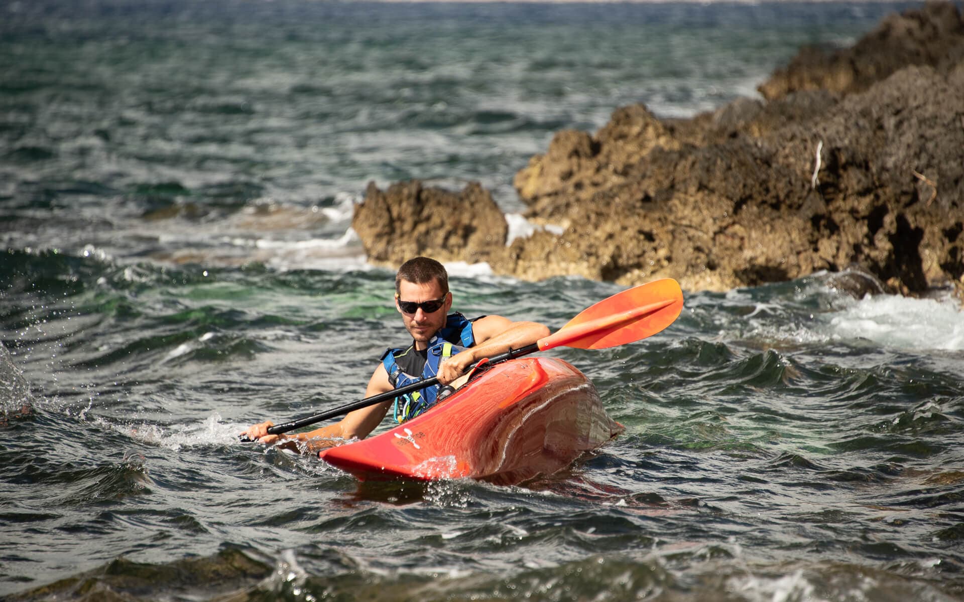 Kayaker in a red boat practicing a low brace maneuver in choppy coastal water.