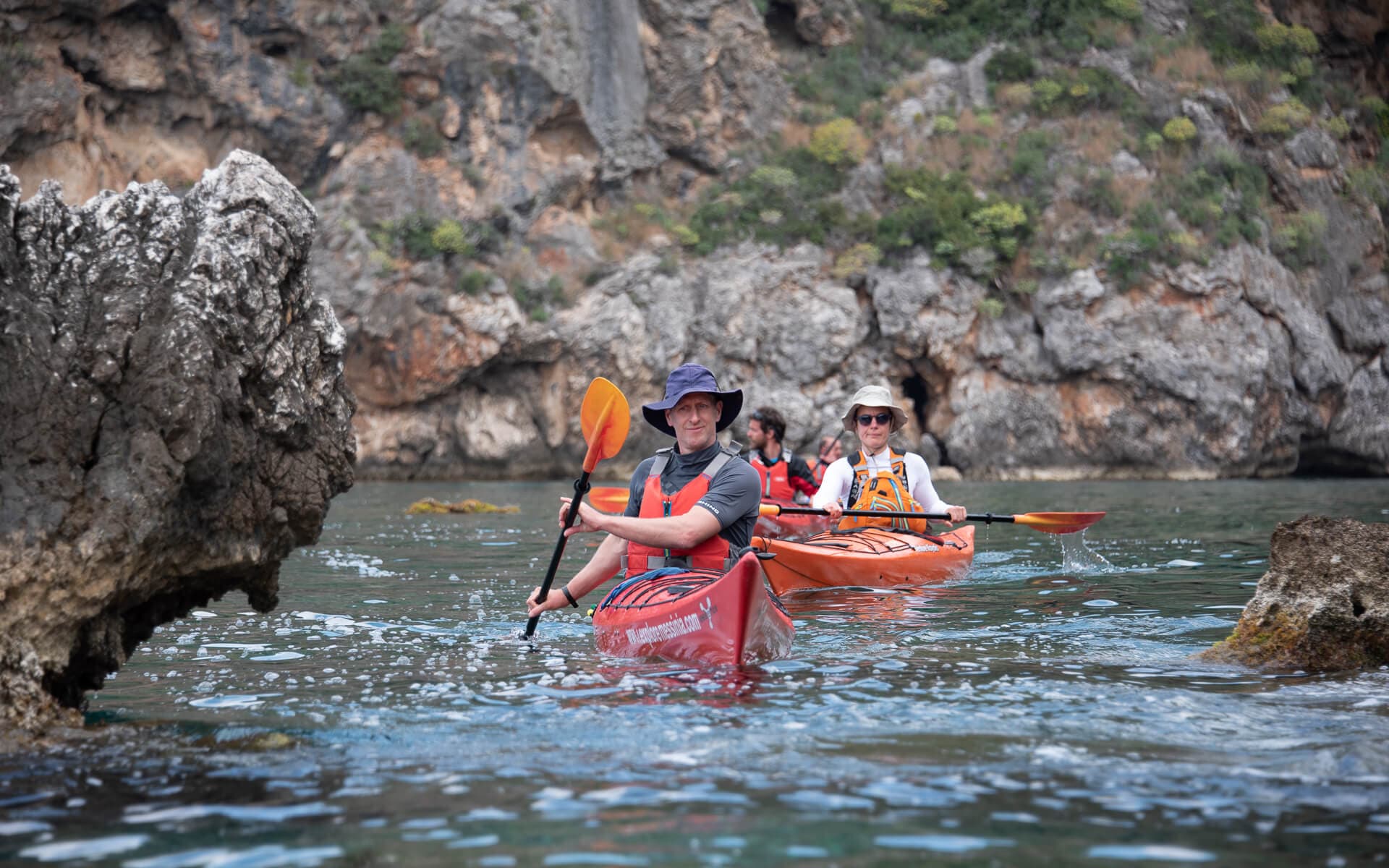 Sea kayakers paddling near dramatic limestone cliffs and sea caves in Messinia.