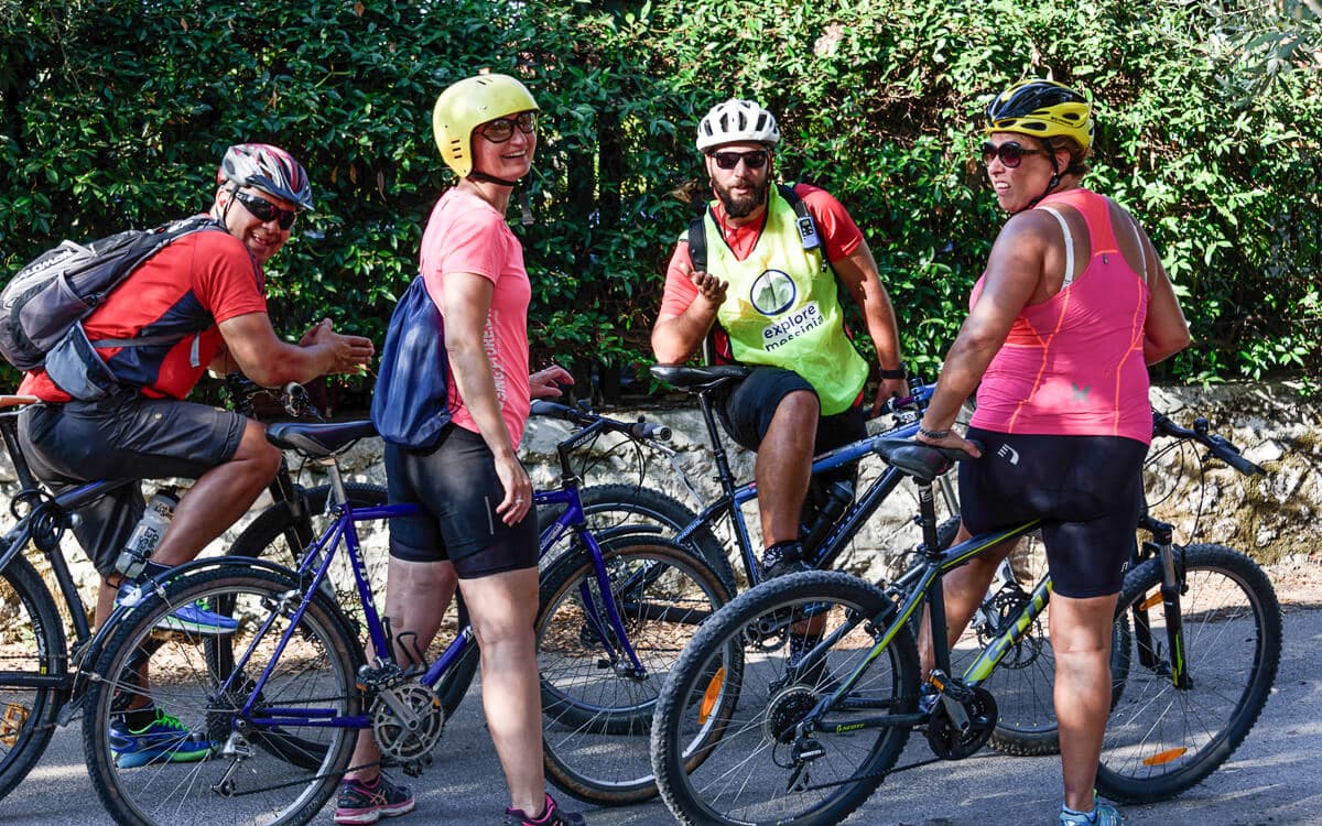 Group of cyclists in helmets pausing with their bikes on a shaded road near Kalamata