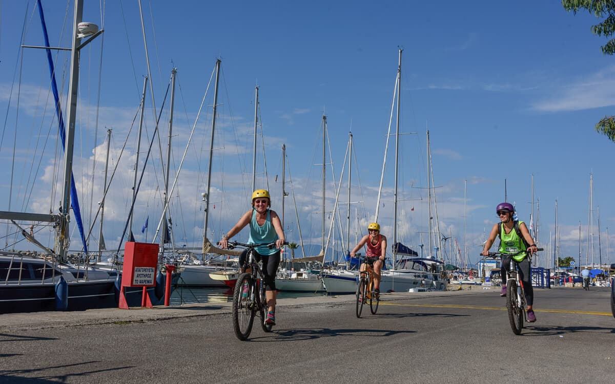 Three cyclists riding along the Kalamata marina past moored sailboats and yachts