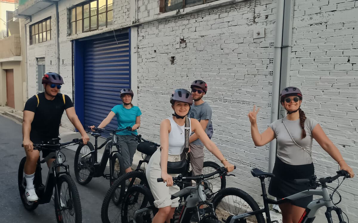 Group of e-bikers smiling beside a whitewashed brick wall on a Kalamata street tour