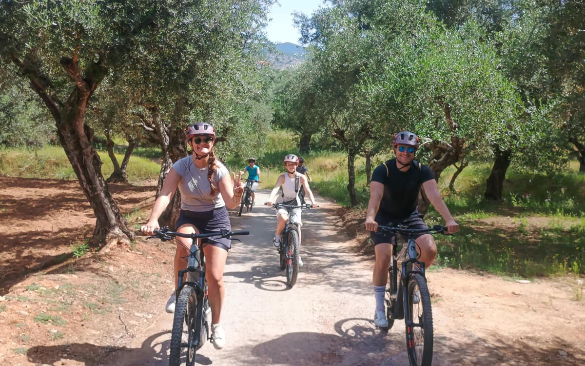 Cyclists riding a dirt path through a sunlit olive grove near Kalamata