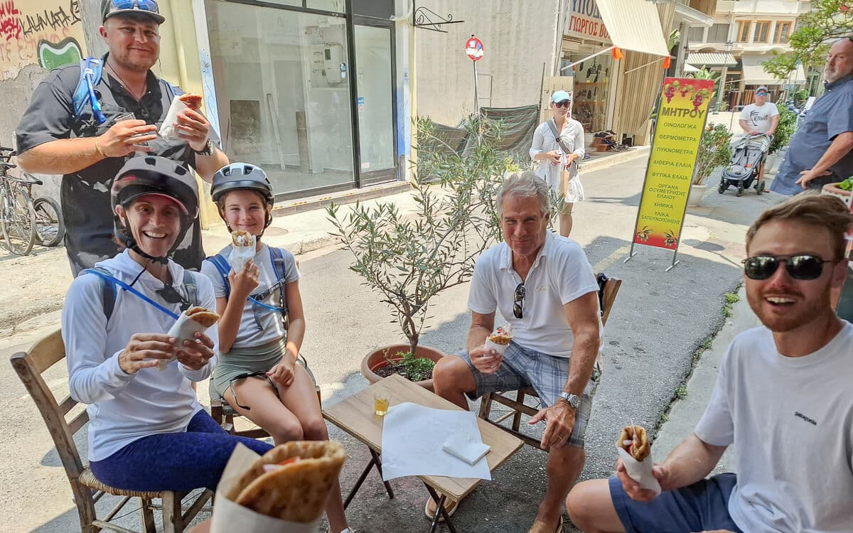 Cyclists in helmets taking a snack break at an outdoor cafe table on a Kalamata bike tour