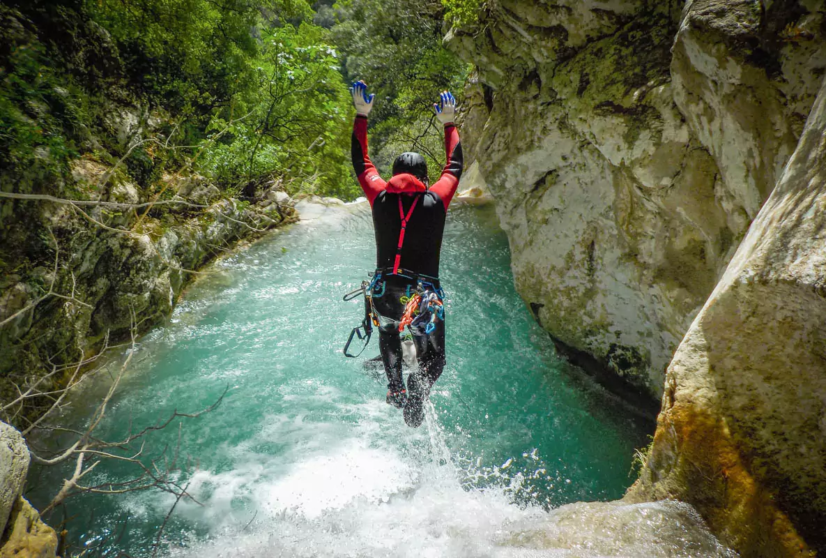 Explore Messinia- Man leaping off a rocky ledge into crystal-clear water at Neda Gorge, showcasing the thrill of canyoning in the Peloponnese. Surrounded by dramatic cliffs and lush greenery, this adventurous moment captures the essence of exploring Greece's natural beauty.