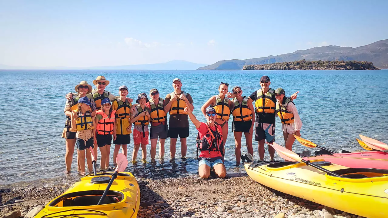 Explore Messinia-A cheerful group posing for a team photo on the beach after a picnic, with their guide and colorful kayaks arranged in the background, celebrating a fun-filled kayaking adventure.