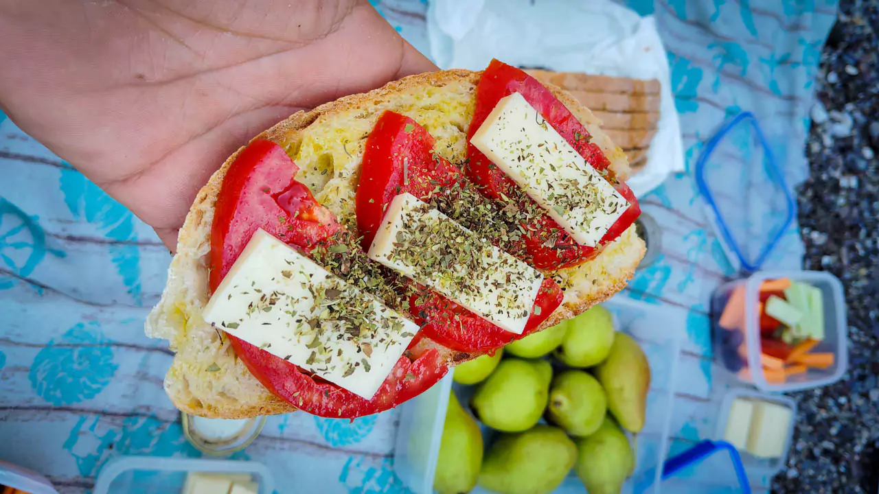 Explore Messinia-A close-up of a slice of fresh bread topped with juicy tomato slices, graviera cheese, a drizzle of extra virgin olive oil, and a sprinkle of oregano, capturing the essence of a traditional Greek delicacy enjoyed during a kayak tour picnic.