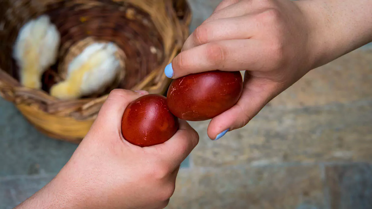 Explore Messinia-Two small hands holding vibrant red Easter eggs during the traditional tsougrisma, where families crack eggs for good luck on Greek Easter.