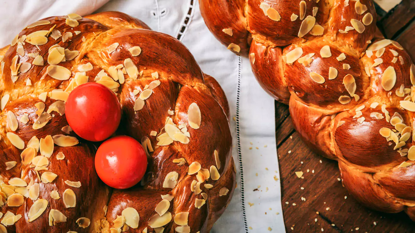 Explore Messinia-Close-up of braided tsoureki, a traditional Greek Easter sweet bread topped with toasted sesame seeds, resting on a wooden table.