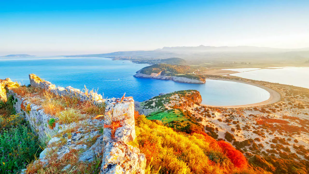 Explore Messinia-A breathtaking view of Voidokilia Beach from Palaiokastro, showcasing its iconic horseshoe shape, golden sands, and turquoise waters, framed by rugged cliffs and lush greenery.