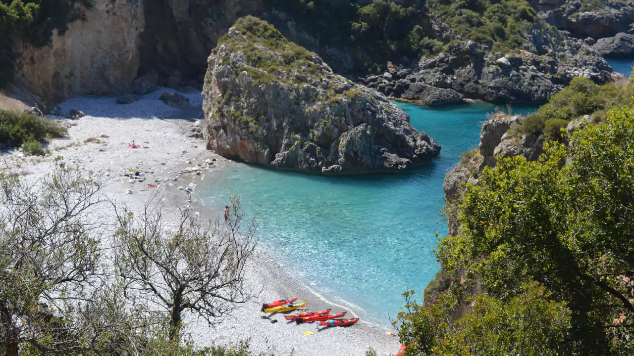 Secluded Foneas beach in Mani Secluded beach in Mani Greece with colorful kayaks on pebbles, rocky cliffs, and turquoise water.